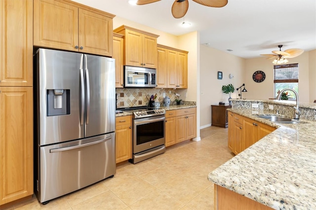 kitchen with appliances with stainless steel finishes, light brown cabinets, backsplash, light stone countertops, and sink