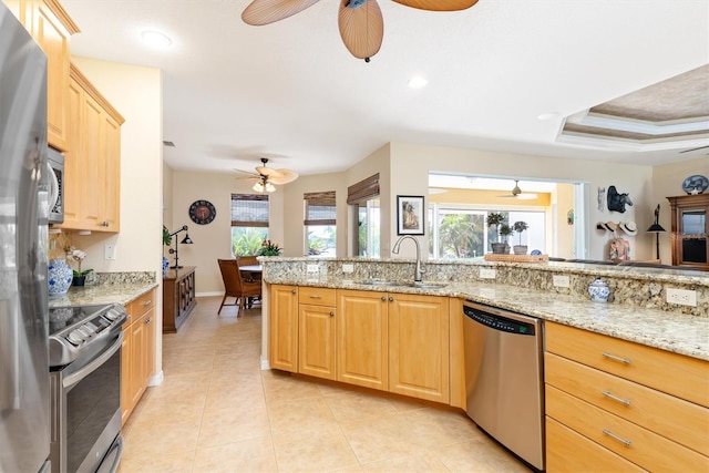 kitchen featuring light stone countertops, appliances with stainless steel finishes, sink, kitchen peninsula, and a tray ceiling