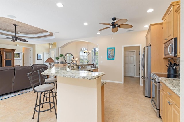 kitchen featuring light stone countertops, a kitchen bar, light brown cabinets, stainless steel appliances, and a tray ceiling