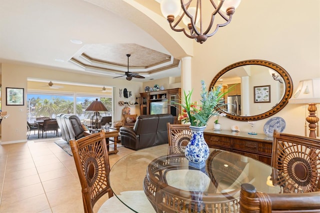 tiled dining space featuring ceiling fan with notable chandelier, decorative columns, and a raised ceiling