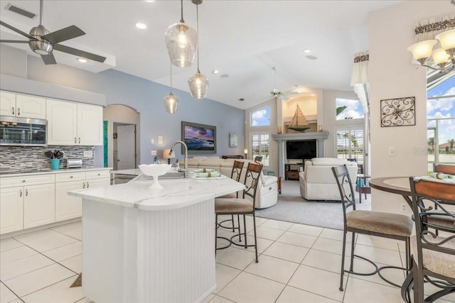 kitchen featuring decorative light fixtures, backsplash, vaulted ceiling, white cabinetry, and light stone counters