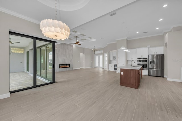 kitchen with white cabinets, ceiling fan, a high end fireplace, stainless steel appliances, and a center island with sink