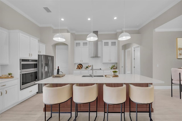 kitchen featuring wall chimney exhaust hood, sink, white cabinetry, decorative light fixtures, and a center island with sink