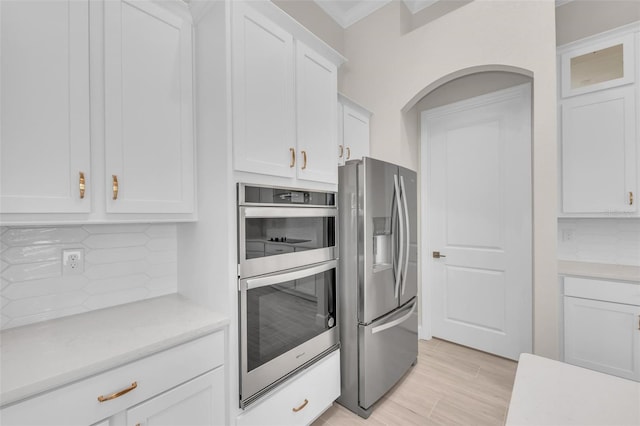 kitchen featuring white cabinetry, stainless steel appliances, ornamental molding, light hardwood / wood-style floors, and decorative backsplash