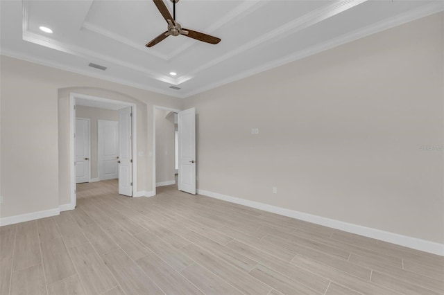 empty room with a raised ceiling, ornamental molding, light wood-type flooring, and ceiling fan