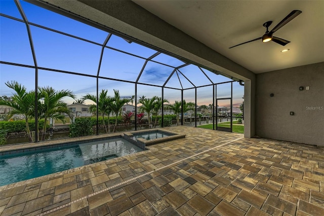 pool at dusk featuring an in ground hot tub, a lanai, ceiling fan, and a patio