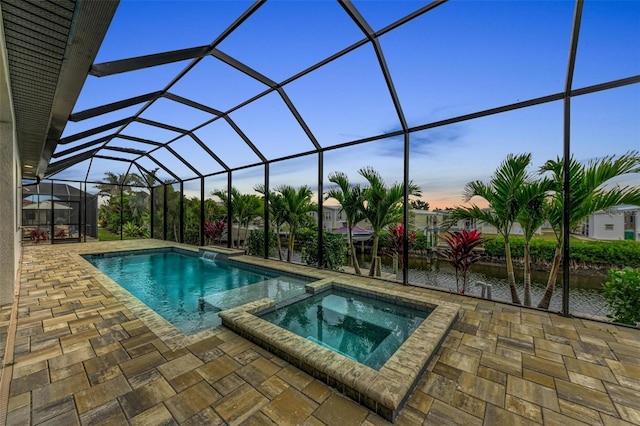 pool at dusk with an in ground hot tub, a water view, a lanai, and a patio