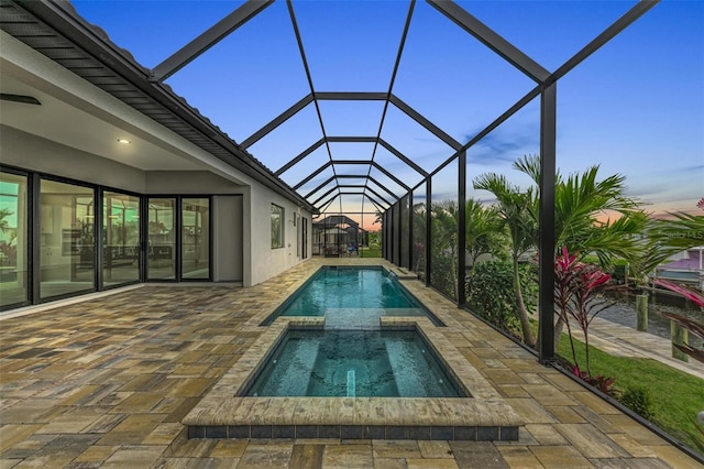 pool at dusk featuring an in ground hot tub, a patio, and glass enclosure