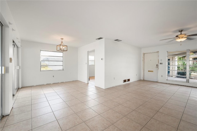 unfurnished room with light tile patterned floors, a healthy amount of sunlight, and ceiling fan with notable chandelier