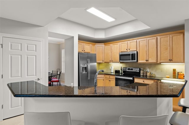 kitchen featuring appliances with stainless steel finishes, a breakfast bar, light brown cabinets, and dark stone countertops