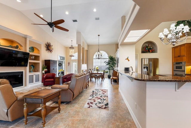 living room featuring ceiling fan with notable chandelier, built in features, and high vaulted ceiling