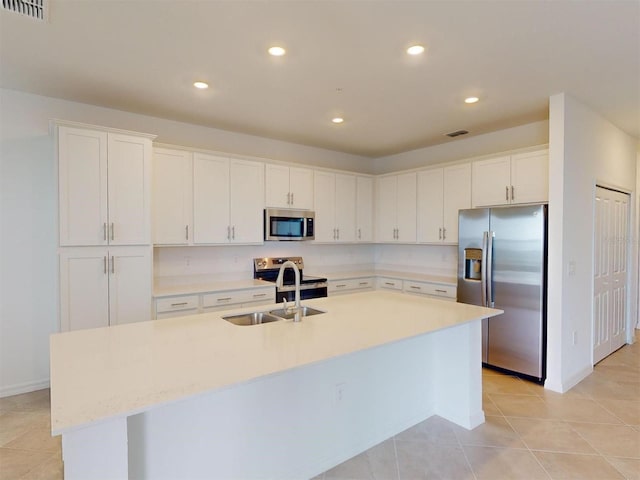 kitchen with light tile patterned floors, white cabinetry, appliances with stainless steel finishes, a kitchen island with sink, and sink