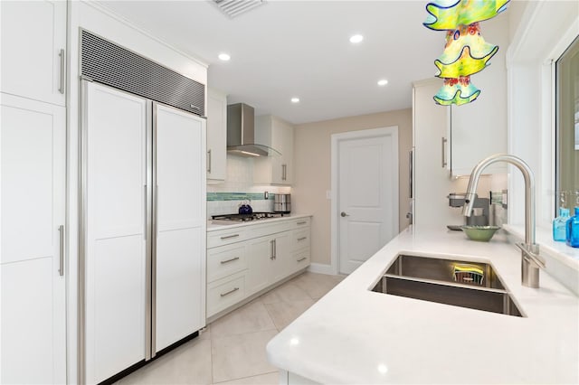 kitchen with wall chimney range hood, sink, stainless steel gas cooktop, white cabinets, and paneled built in fridge