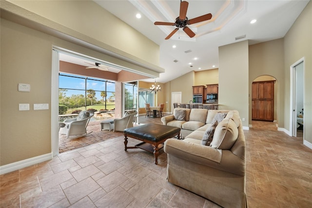 living room with a raised ceiling, a towering ceiling, crown molding, and ceiling fan with notable chandelier