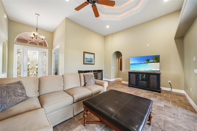 living room with ceiling fan with notable chandelier, a tray ceiling, and ornamental molding