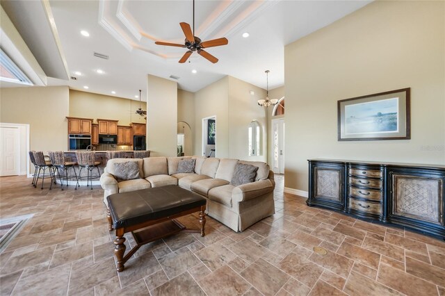 living room with crown molding, ceiling fan with notable chandelier, a high ceiling, and a tray ceiling