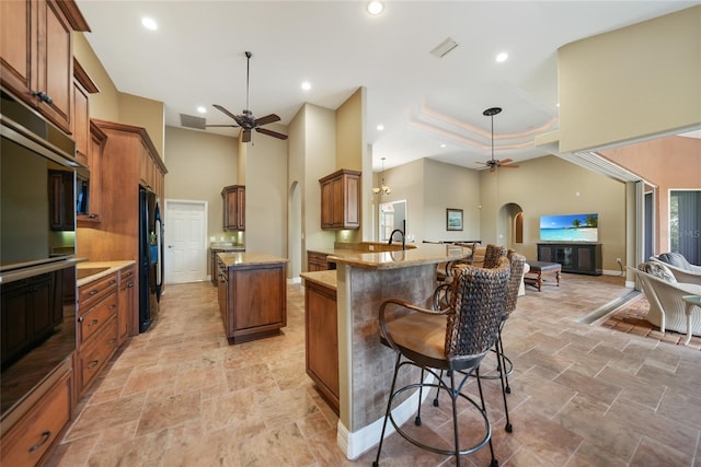 kitchen featuring ceiling fan, a raised ceiling, kitchen peninsula, and a breakfast bar area