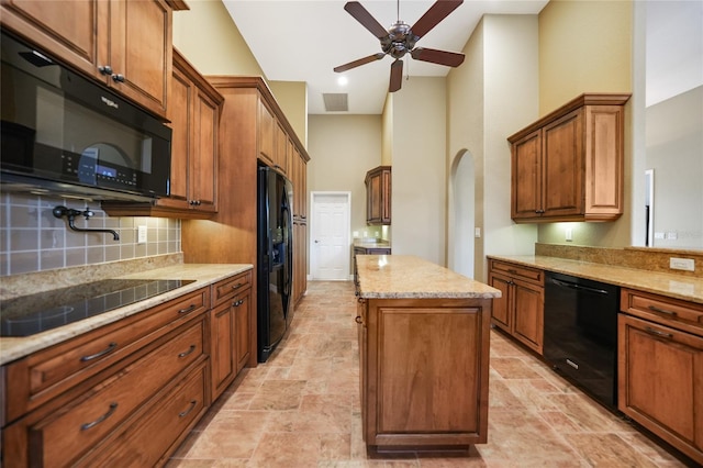 kitchen featuring ceiling fan, backsplash, a kitchen island, black appliances, and light stone countertops