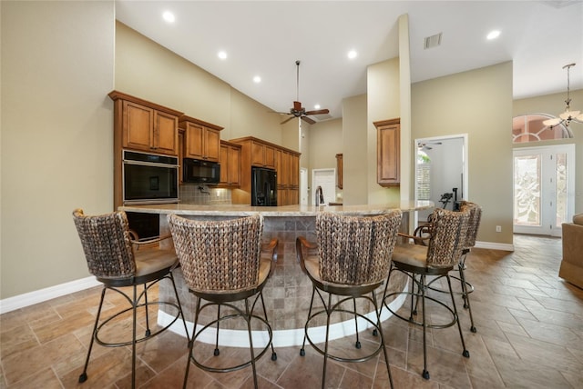 kitchen with tasteful backsplash, black appliances, kitchen peninsula, a kitchen bar, and ceiling fan with notable chandelier