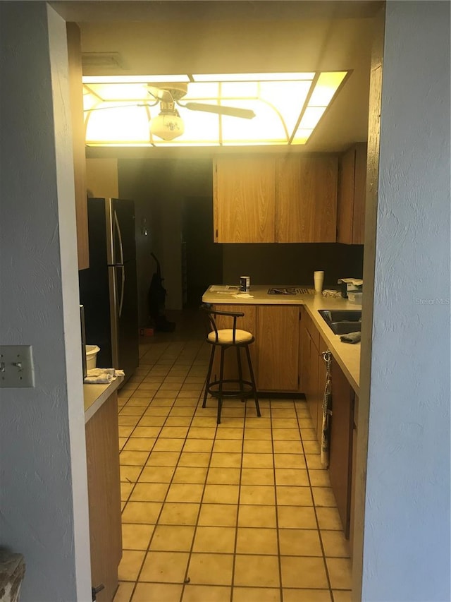 kitchen featuring a kitchen bar, sink, light tile patterned floors, stainless steel fridge, and kitchen peninsula