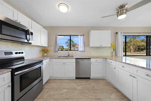 kitchen with appliances with stainless steel finishes, white cabinetry, sink, decorative backsplash, and light stone countertops