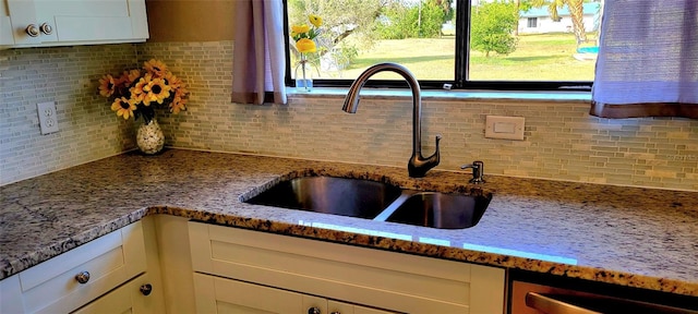 kitchen featuring sink, light stone counters, white cabinets, and backsplash