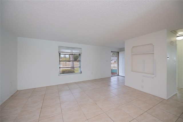 unfurnished room featuring built in shelves, light tile patterned flooring, and a textured ceiling