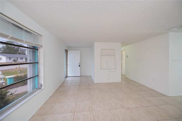 spare room with a wealth of natural light, a textured ceiling, and light tile patterned flooring