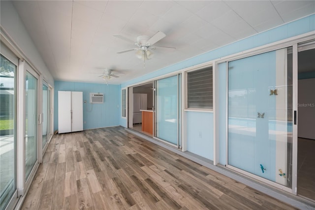 unfurnished sunroom with ceiling fan, a wall mounted AC, and plenty of natural light