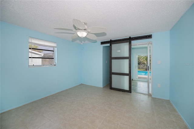 spare room featuring ceiling fan, a textured ceiling, and a barn door