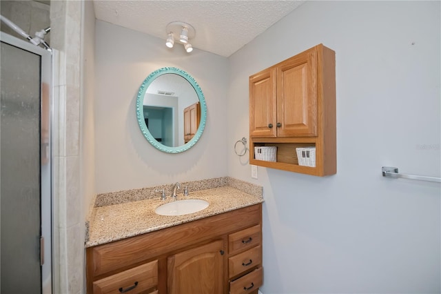 bathroom featuring a shower with shower door, a textured ceiling, and vanity