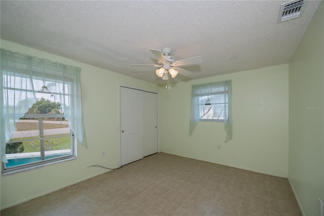 unfurnished bedroom featuring a textured ceiling, ceiling fan, a closet, and multiple windows