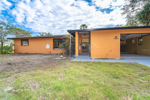 rear view of property with a carport, a lawn, and driveway