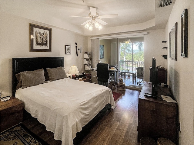 bedroom featuring dark hardwood / wood-style floors, ceiling fan, a raised ceiling, and access to outside