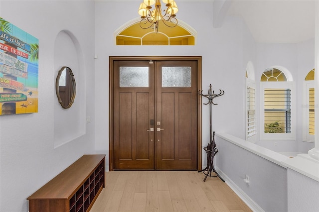 entryway featuring a notable chandelier, a towering ceiling, and light hardwood / wood-style flooring