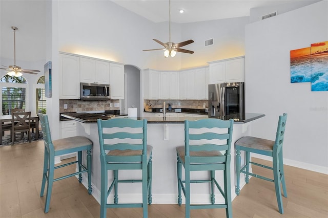 kitchen featuring a breakfast bar, kitchen peninsula, white cabinetry, appliances with stainless steel finishes, and high vaulted ceiling