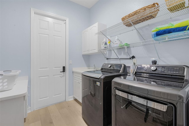 clothes washing area with washing machine and dryer, sink, light hardwood / wood-style floors, and cabinets