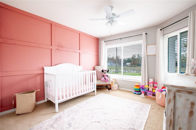 bedroom with ceiling fan, multiple windows, carpet floors, and a crib