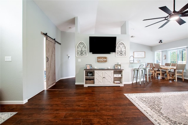 unfurnished living room with ceiling fan, a barn door, vaulted ceiling, and dark wood-type flooring