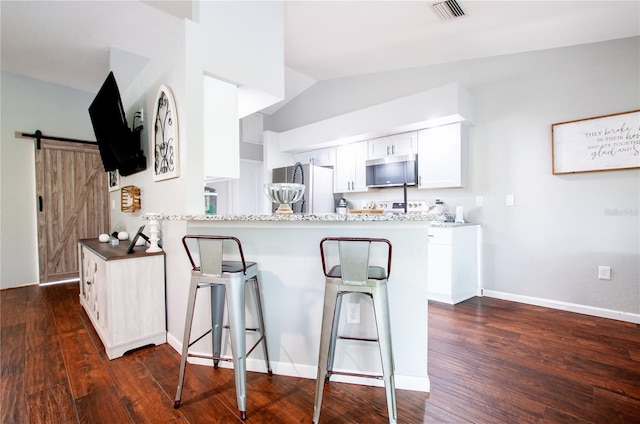 kitchen with a barn door, kitchen peninsula, stainless steel appliances, and white cabinetry