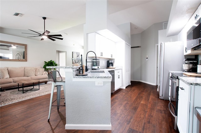 kitchen with white cabinets, dark wood-type flooring, stainless steel appliances, a kitchen breakfast bar, and light stone counters