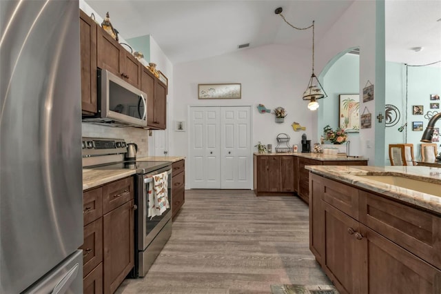 kitchen with appliances with stainless steel finishes, tasteful backsplash, hanging light fixtures, vaulted ceiling, and light hardwood / wood-style flooring