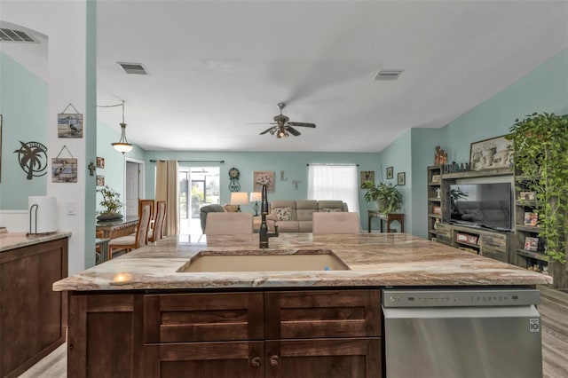 kitchen with ceiling fan, stainless steel dishwasher, sink, a kitchen island with sink, and light stone countertops