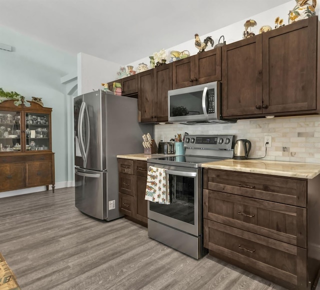 kitchen with light wood-type flooring, stainless steel appliances, dark brown cabinets, and tasteful backsplash