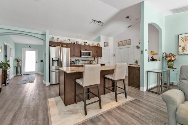 kitchen with lofted ceiling, a center island with sink, hardwood / wood-style flooring, appliances with stainless steel finishes, and a breakfast bar area