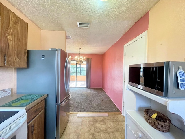 kitchen featuring light colored carpet, hanging light fixtures, appliances with stainless steel finishes, a textured ceiling, and a chandelier