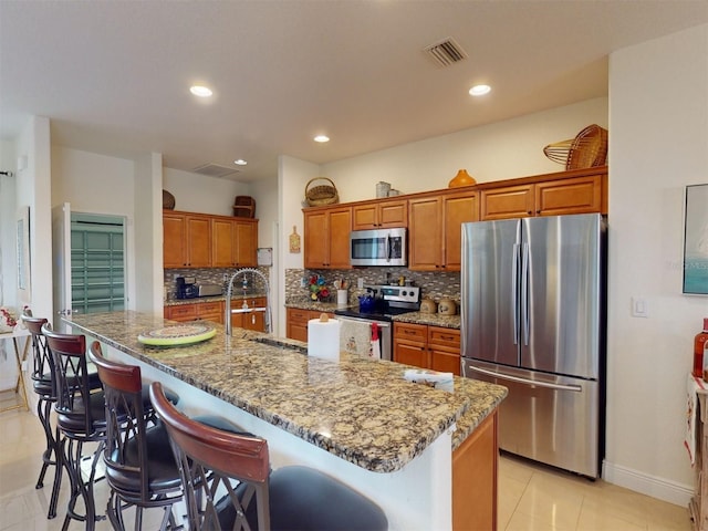 kitchen featuring a kitchen bar, a large island, appliances with stainless steel finishes, light tile patterned flooring, and light stone counters