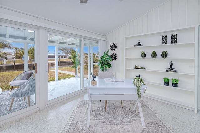 home office with built in shelves, vaulted ceiling, and wooden walls