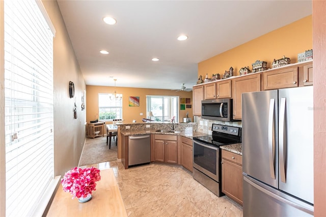 kitchen with pendant lighting, kitchen peninsula, sink, appliances with stainless steel finishes, and light stone counters