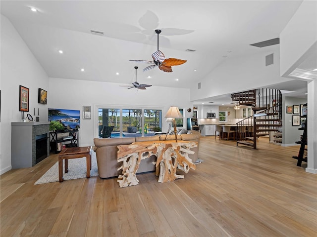 living room featuring light wood-type flooring, a tiled fireplace, ceiling fan, and high vaulted ceiling